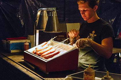 A vendor places corn dogs under a heat lamp at the food court.