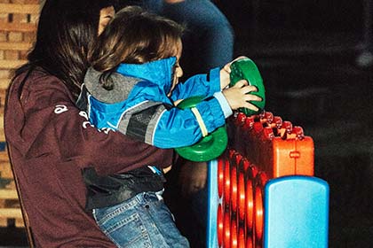 A mom lifts her daughter so she can drop a game piece into the oversized connect 4 board.