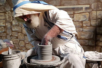 A volunteer dressed in period clothing spins a pot on a wheel at the Town of Bethlehem.