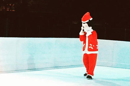 A mascot dressed as Mickey Mouse in Santa clothse skates at the ice rink.
